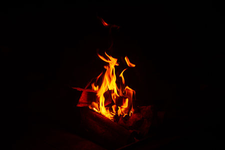 Bright orange flames from a wood campfire glowing in the dark, creating a cozy and rustic outdoor...