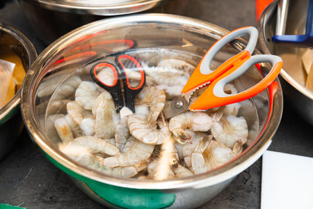 Bowl filled with raw shrimp soaking in water, accompanied by kitchen scissors for cleaning and preparation in a cooking setting.の写真素材