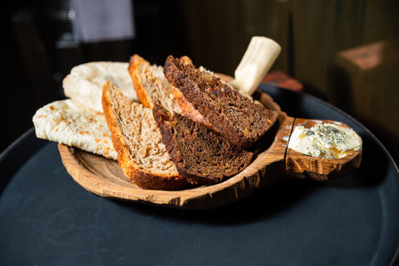 Artisan bread slices and flatbread served on a wooden tray with a side of whipped herb butter for...