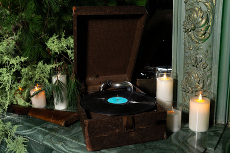 Old-fashioned vinyl record player surrounded by burning candles and pine branches, creating a cozy...