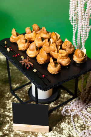 Gourmet profiterole-style appetizers served on a decorative black slate tray with spices, pearls, and luxury party decor.の写真素材