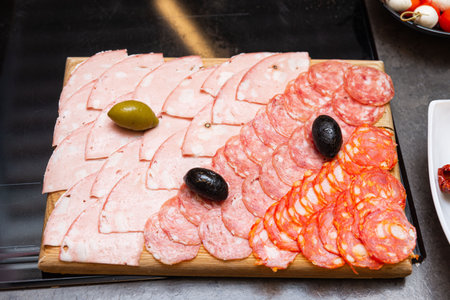 Selection of sliced cured meats including salami, mortadella, and chorizo arranged on a wooden board with olives.の写真素材