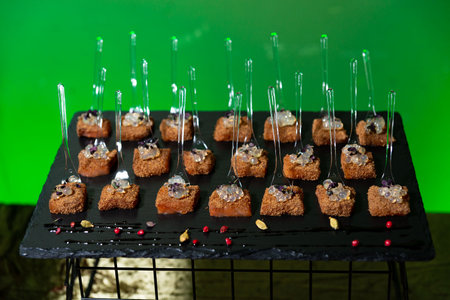 Plated gourmet appetizers topped with translucent garnish pearls on black slate, presented with cocktail forks for upscale events.の写真素材