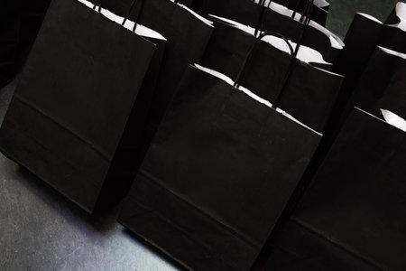 Group of elegant black paper bags with handles, arranged for guests at a corporate or promotional event as gift packages.の写真素材