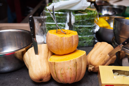 Halved pumpkins with utensils and knives in a busy kitchen setup, ready for preparation in a...