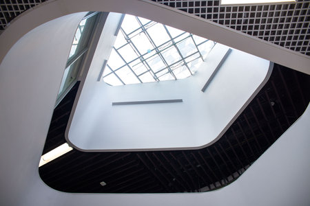 Looking upward at a bright skylight in a contemporary atrium featuring smooth white walls and bold geometric lines.の写真素材