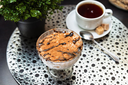Classic Italian tiramisu served in a glass dish, topped with cocoa powder and chocolate drizzle,...