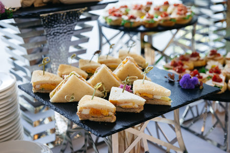 Elegant display of small triangle tea sandwiches with various fillings, served on a black slate platter at a catered event.の写真素材