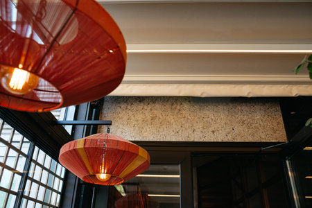 Stylish interior lighting featuring red and yellow woven pendant lamps hanging in a contemporary room with large windows and ceiling beams.の写真素材