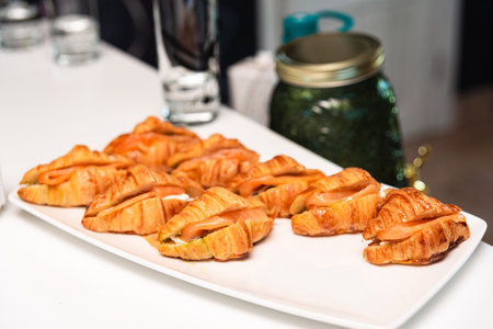 Freshly baked mini croissants filled with smoked salmon and cream cheese, served on a white platter...