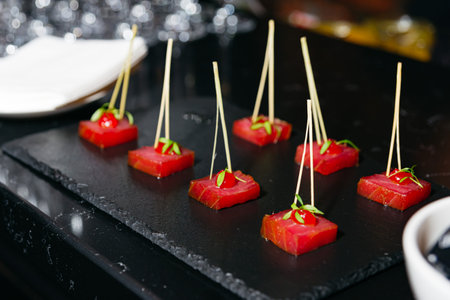 Elegant bite-sized tuna hors d'oeuvres served on skewers with garnish, arranged on a black slate...