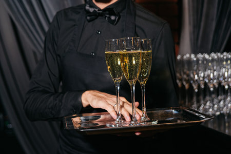 A waiter in black attire carries a tray with glasses of champagne during a formal celebration or upscale gathering.の写真素材