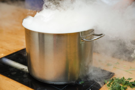 Large stainless steel pot on stove emitting heavy steam, overflowing during intense boil, indicating active cooking process in kitchen.の写真素材