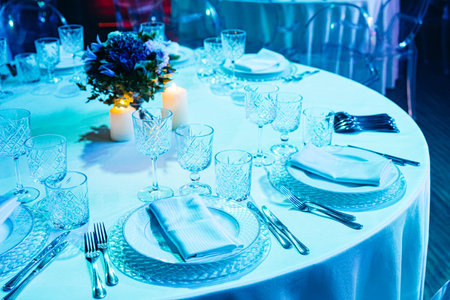 Beautiful round banquet table with crystal glasses, floral centerpiece, and candles, prepared for a formal dinner or wedding reception.の写真素材