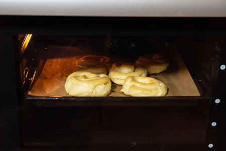 Close-up of raw pretzel dough baking in the oven on parchment paper, showing the rising process during preparation.の写真素材