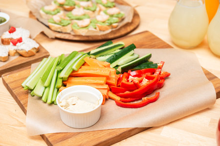 Freshly sliced carrots, celery, cucumber, and bell peppers arranged on a wooden board with a bowl of...
