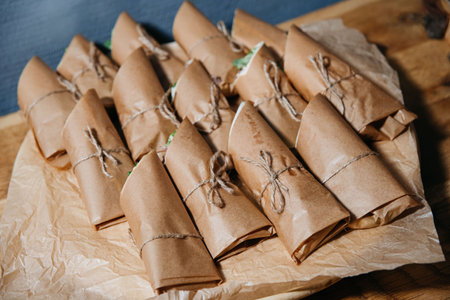 Multiple sandwiches neatly wrapped in brown paper and twine, presented on parchment for...