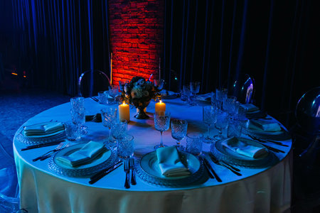 Luxurious round dinner table arranged for an evening event with crystal glasses, white linens, candles, and floral centerpiece.の写真素材