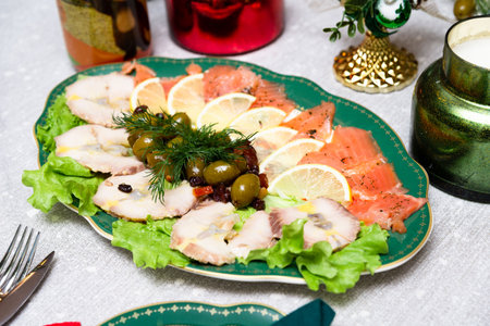 Elegant holiday platter with smoked fish slices, lemon wedges, green olives, herbs, and lettuce served on a festive table.の写真素材