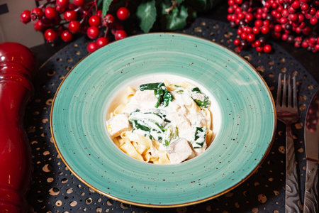 Tagliatelle pasta served with creamy white sauce, tender chicken pieces, and fresh spinach, plated in a turquoise bowl.の写真素材