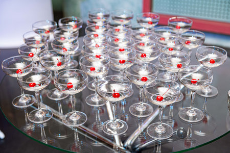 Dozens of clear cocktail glasses with red cherries arranged on a glass table, perfect for upscale party or celebration visuals.の写真素材