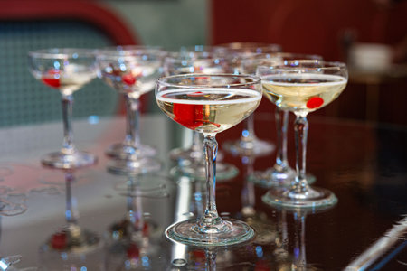 Elegant coupe glasses filled with champagne and red cherries, arranged on a glossy table, perfect for events or celebrations.の写真素材