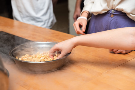 A person reaches into a metal bowl filled with caramel popcorn, surrounded by a smoky vapor on a wooden table.の写真素材