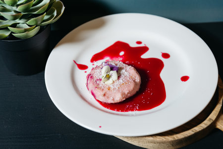 Artfully plated pink mousse dessert with vibrant berry sauce, topped with shredded coconut and...
