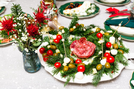Creative Christmas-themed platter arranged like a wreath with olives, tomatoes, cheese, mozzarella, and salami on evergreen sprigs.の写真素材