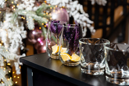 Empty cocktail glasses garnished with lemon slices and purple basil, set against a festive Christmas tree background with lights.の写真素材