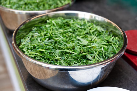 Large bowl filled with fresh, chopped arugula leaves prepared for salad or cooking, displayed in a...