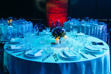 Luxury banquet hall with round tables set for a formal event, featuring crystal glassware, candles,...
