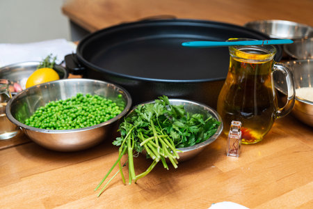 A kitchen scene with peas, parsley, saffron oil, and other ingredients laid out on a wooden counter beside a large pan.の写真素材