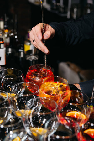 Close-up of a bartender stirring Aperol spritz cocktails with orange slices and ice at a professional bar setup.の写真素材