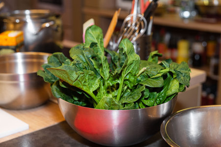 Raw spinach leaves placed in a stainless steel bowl, ready for use in cooking or salad preparation in a kitchen setting.の写真素材
