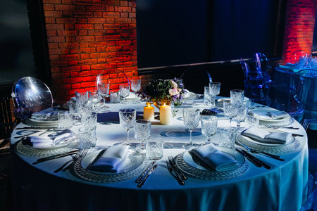 A beautifully set round table with crystal glassware, white linens, candles, and floral centerpiece, prepared for a formal evening dinner.の写真素材