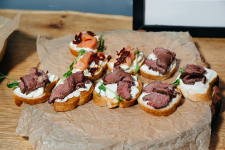 Selection of elegant bite-sized canapÃ©s with roast beef, smoked salmon, cream cheese, and greens served on toasted baguette slices.の写真素材