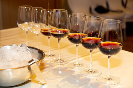Multiple wine glasses filled with red wine on a table, prepared for an event or wine tasting, with ice bucket nearby.の写真素材