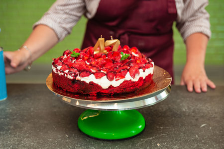 Festive strawberry birthday cake with whipped cream and number candles on a rotating cake stand, perfect for celebrations and parties.の写真素材