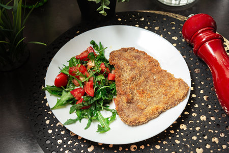 Crispy breaded schnitzel served alongside a fresh arugula and tomato salad on a white plate with elegant presentation.の写真素材