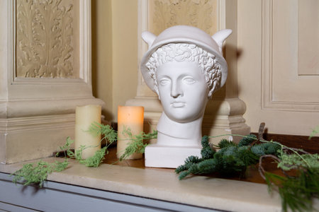White bust sculpture of a Greek god styled with candles, pine branches, and soft greenery for elegant seasonal decoration.の写真素材