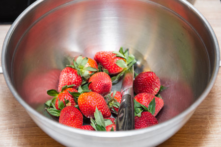 Ripe strawberries with green stems in a metal bowl with a kitchen knife, ready for preparation or dessert recipes.の写真素材