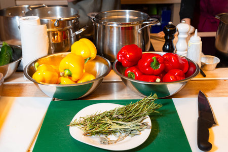 Colorful red and yellow bell peppers with fresh rosemary and sage on a prep table in a professional kitchen setting.の写真素材