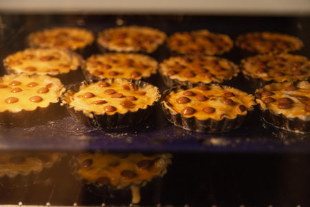 Close-up view of multiple small tarts with chocolate chips baking inside an oven, golden and deliciously rising in trays.の写真素材