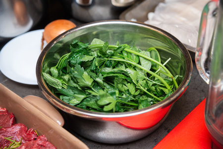 Close-up of freshly picked parsley and basil leaves placed in a stainless steel bowl, ready for cooking or garnishing dishes.の写真素材