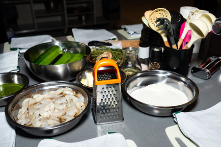 A kitchen countertop with fresh shrimp, zucchini, flour, herbs, and cooking tools prepared for a gourmet cooking session.の写真素材