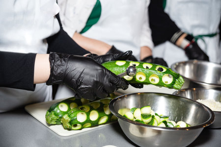 Close-up of chefs using melon ballers to hollow fresh zucchinis, preparing vegetables for cooking in a professional kitchen setting.の写真素材