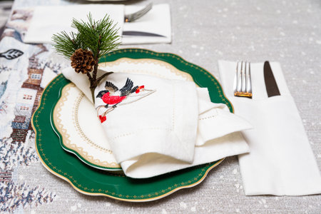 Festive holiday table setup with green and gold plates, embroidered bird napkin, and pinecone accent for Christmas dinner.の写真素材