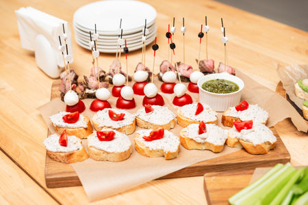 Assorted appetizers on a wooden board including bruschetta with cream spread and tomato skewers with mozzarella and meat.の写真素材