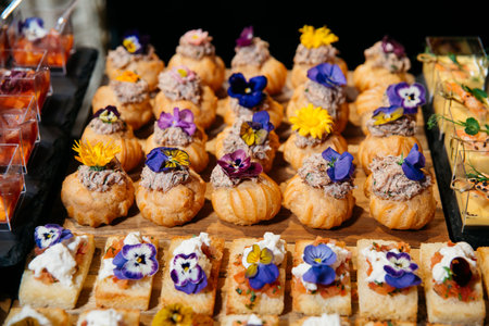 Elegant bite-sized appetizers featuring cream puffs and crostini, artfully decorated with colorful edible flowers for a festive event.の写真素材